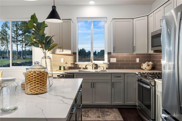 kitchen featuring light stone countertops, appliances with stainless steel finishes, gray cabinetry, sink, and hanging light fixtures