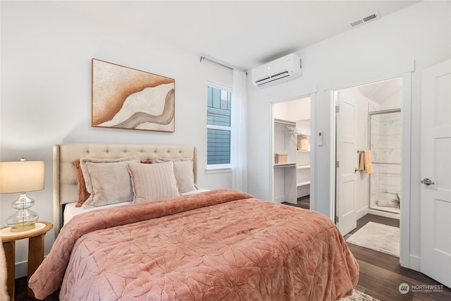 bedroom with a spacious closet, dark hardwood / wood-style flooring, an AC wall unit, and connected bathroom