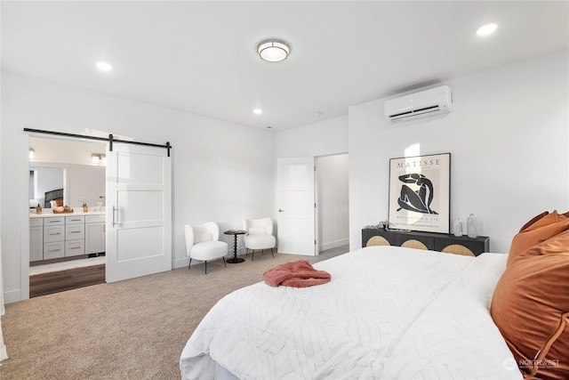 bedroom featuring an AC wall unit, a barn door, carpet flooring, and ensuite bath