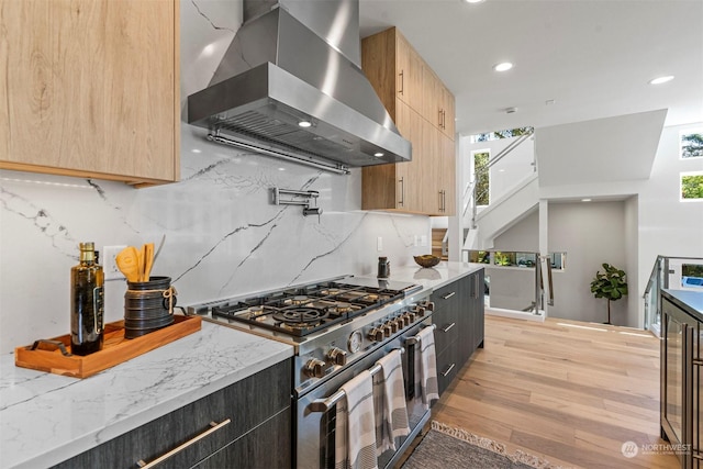 kitchen with island exhaust hood, light brown cabinetry, light stone counters, high end stove, and light hardwood / wood-style flooring