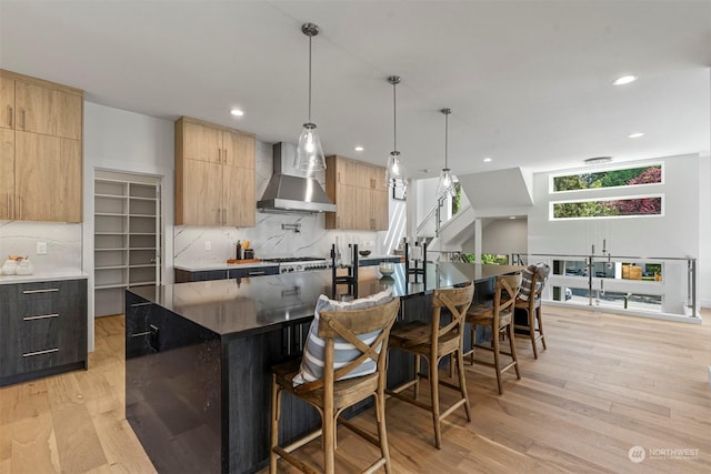 kitchen featuring tasteful backsplash, wall chimney exhaust hood, a spacious island, light hardwood / wood-style flooring, and hanging light fixtures