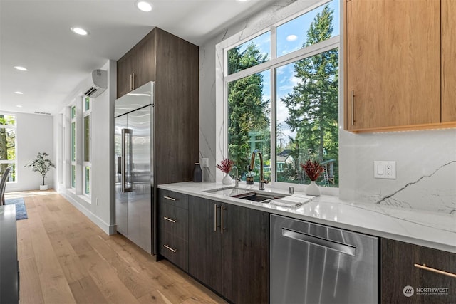 kitchen with sink, light stone counters, a wall mounted AC, appliances with stainless steel finishes, and light wood-type flooring