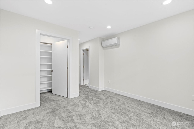 unfurnished bedroom featuring a walk in closet, light colored carpet, a wall unit AC, and a closet