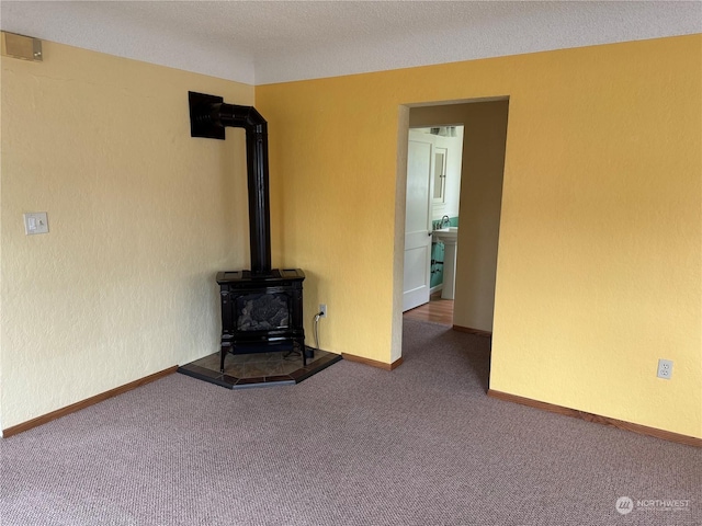 unfurnished living room featuring a wood stove, carpet floors, and a textured ceiling