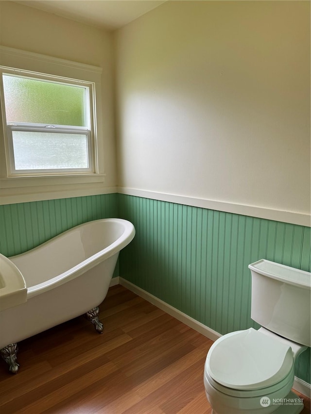 bathroom with a tub to relax in, toilet, and hardwood / wood-style flooring