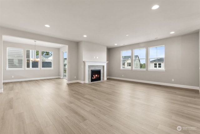 unfurnished living room featuring a notable chandelier, light wood-type flooring, and a wealth of natural light