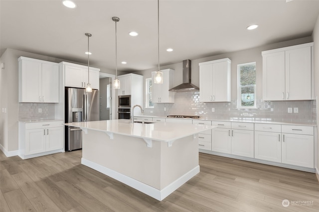 kitchen with light wood-type flooring, wall chimney exhaust hood, white cabinetry, and stainless steel appliances