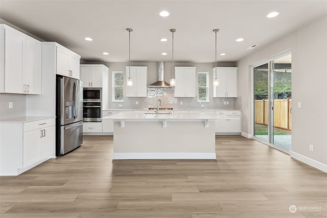 kitchen featuring white cabinets, pendant lighting, a kitchen island with sink, wall chimney range hood, and stainless steel appliances