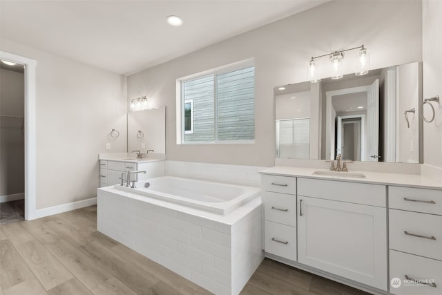 bathroom featuring tiled tub, vanity, and wood-type flooring