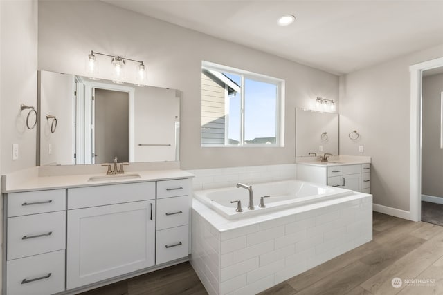 bathroom with tiled tub, wood-type flooring, and vanity