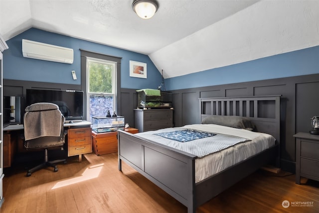 bedroom with an AC wall unit, lofted ceiling, and light hardwood / wood-style floors