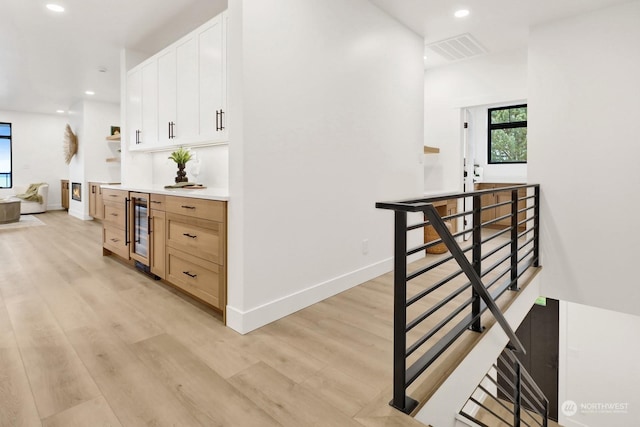 interior space featuring white cabinetry, light brown cabinetry, wine cooler, and light hardwood / wood-style flooring