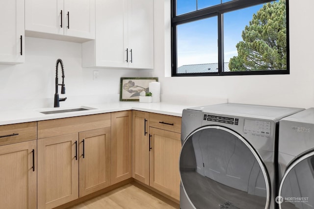 clothes washing area with cabinets, a healthy amount of sunlight, washer and dryer, and sink