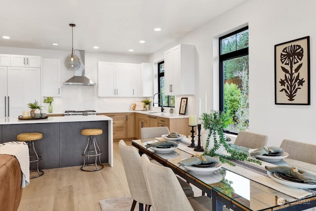 kitchen with wall chimney exhaust hood, sink, a breakfast bar area, pendant lighting, and white cabinets