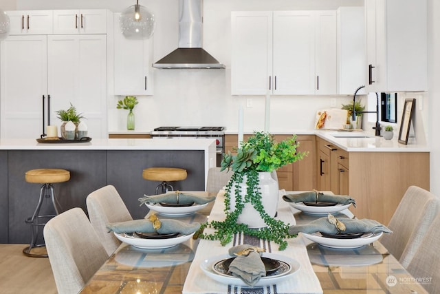 kitchen featuring wall chimney range hood, sink, hanging light fixtures, and white cabinets