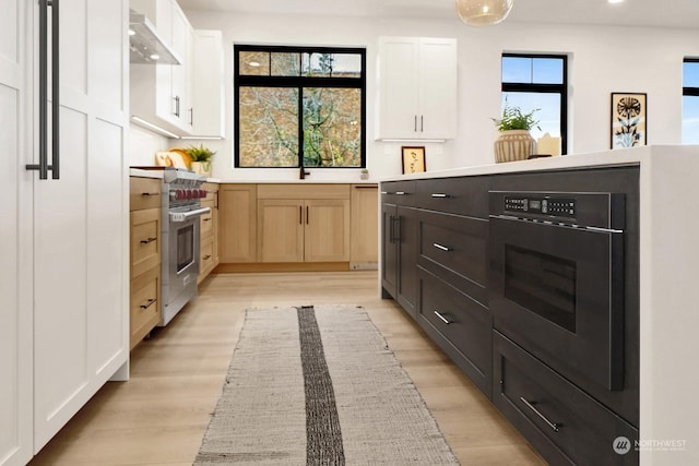 kitchen with white cabinets, wall chimney range hood, high end stainless steel range, and light brown cabinets