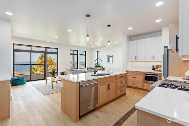 kitchen with pendant lighting, white cabinetry, dishwasher, sink, and a center island with sink