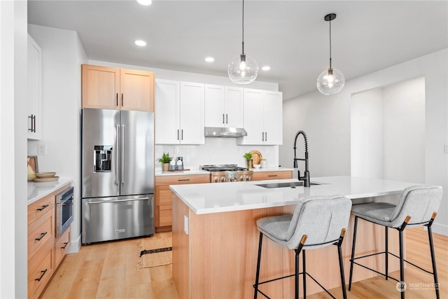 kitchen with sink, high end refrigerator, range, a kitchen island with sink, and white cabinets