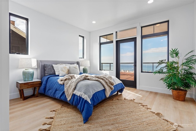 bedroom with access to outside, light hardwood / wood-style floors, and a water view