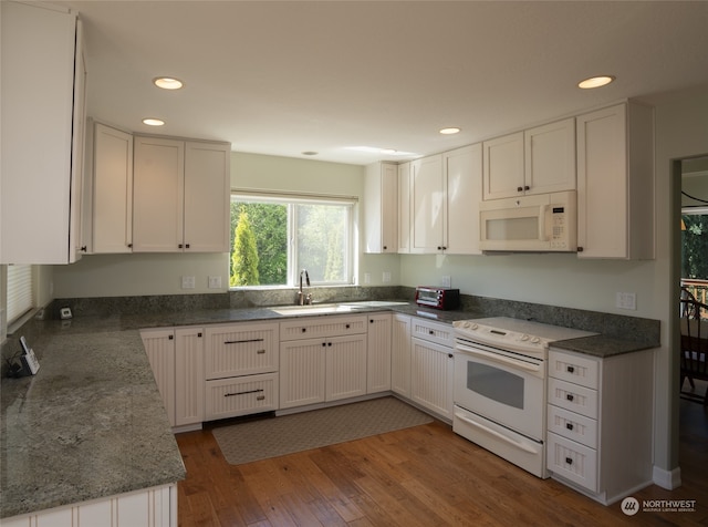 kitchen with hardwood / wood-style floors, white cabinetry, dark stone countertops, sink, and white appliances