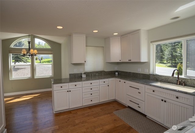 kitchen with dark hardwood / wood-style floors, dark stone counters, sink, white cabinets, and a chandelier