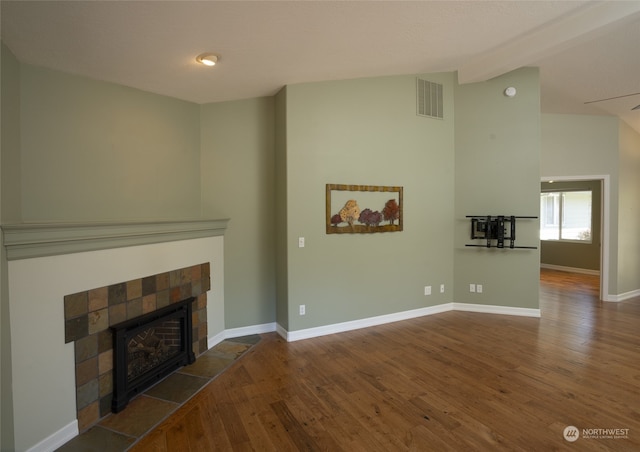 unfurnished living room with vaulted ceiling with beams, dark hardwood / wood-style flooring, and a tiled fireplace