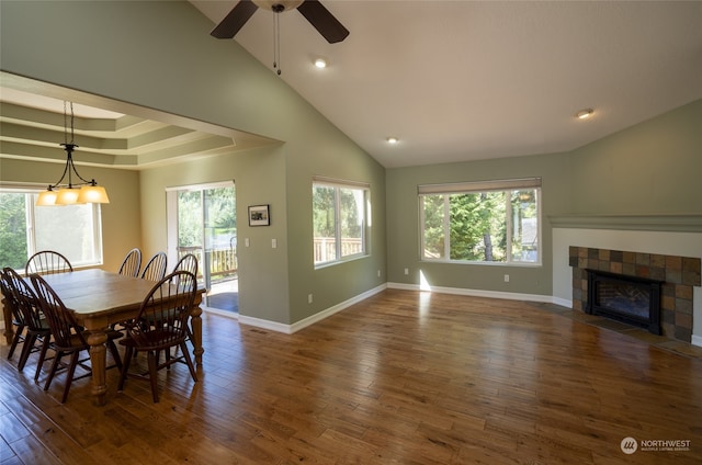 dining room featuring a towering ceiling, a tiled fireplace, ceiling fan, and dark hardwood / wood-style flooring