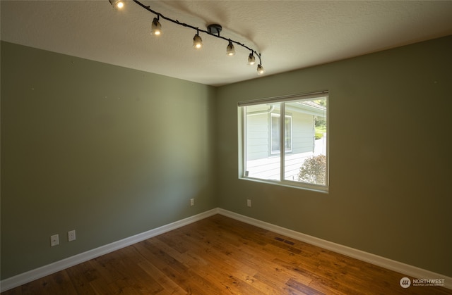 spare room with a textured ceiling, track lighting, and wood-type flooring