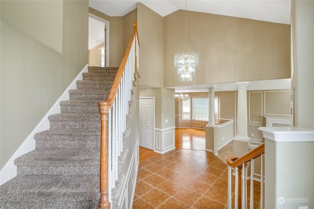 stairway featuring tile patterned flooring, ornate columns, high vaulted ceiling, and a chandelier