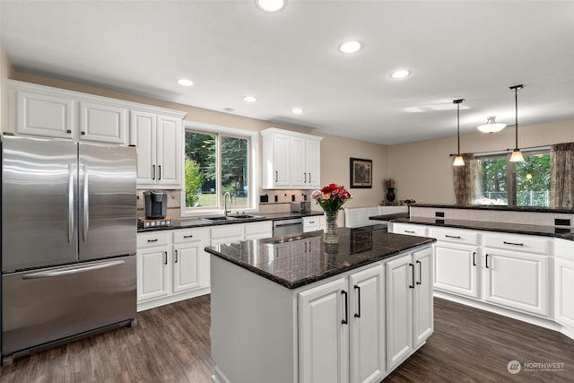 kitchen with stainless steel appliances, white cabinetry, sink, and dark stone counters