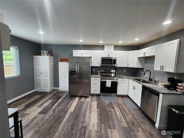 kitchen with a sink, dark stone countertops, stainless steel appliances, white cabinetry, and dark wood-style flooring