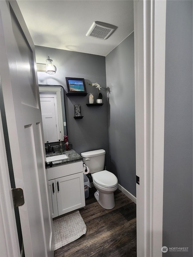 bathroom featuring visible vents, baseboards, toilet, wood finished floors, and vanity