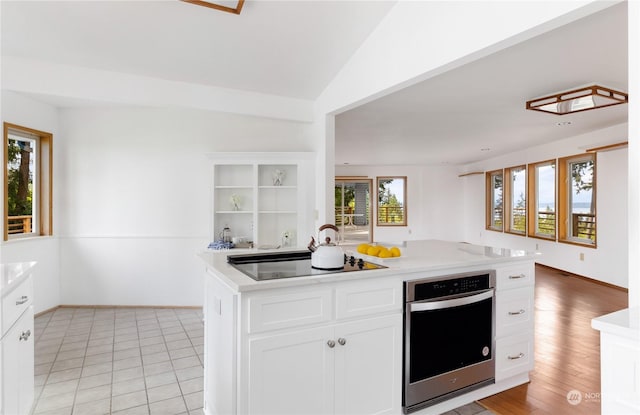 8167 Possession Ridge Ln, Clinton, WA 98236 - kitchen with lofted ceiling, white cabinets, stainless steel oven, black electric stovetop, and light tile patterned floors
