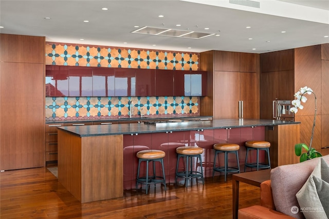 bar with sink, dark stone countertops, backsplash, and dark wood-type flooring