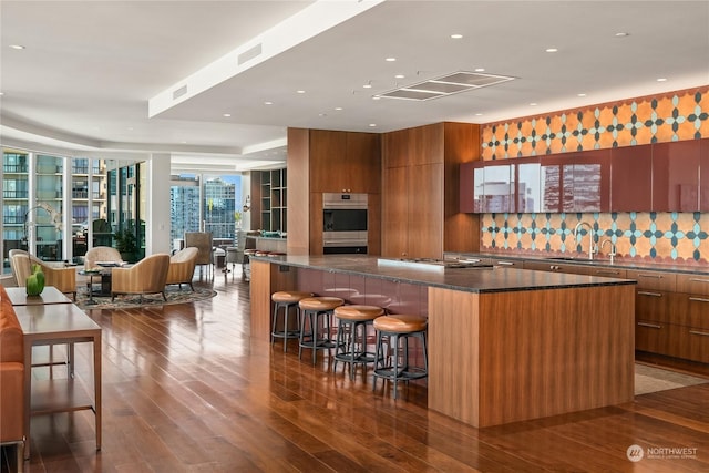 bar featuring backsplash, stainless steel appliances, dark wood-type flooring, sink, and dark stone countertops