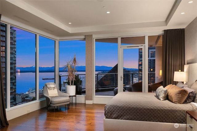 bedroom featuring hardwood / wood-style floors, a tray ceiling, a water and mountain view, and access to outside