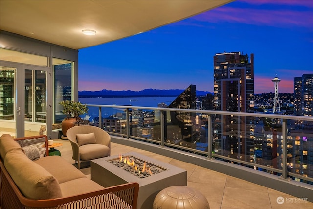 balcony at dusk with an outdoor living space with a fire pit and a water view