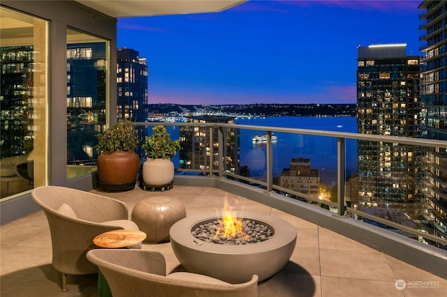 balcony at dusk featuring a water view and an outdoor fire pit