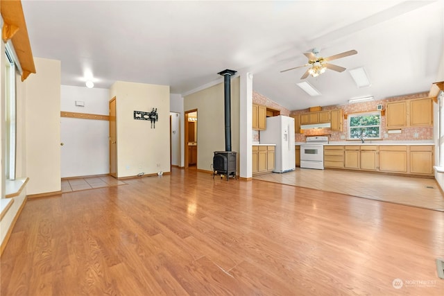 unfurnished living room with ceiling fan, a wood stove, light hardwood / wood-style flooring, and vaulted ceiling