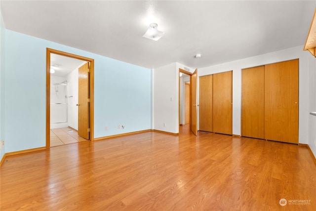 unfurnished bedroom with two closets, ensuite bathroom, and light hardwood / wood-style floors