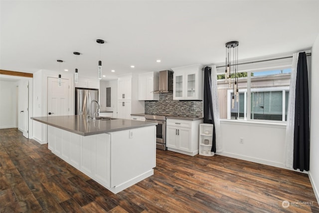 kitchen featuring a large island with sink, wall chimney range hood, appliances with stainless steel finishes, decorative light fixtures, and white cabinetry