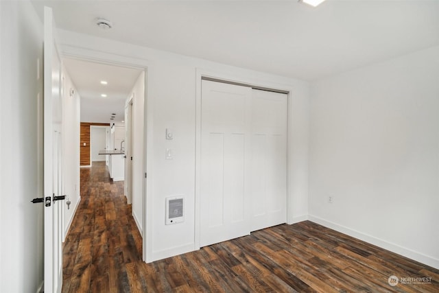 unfurnished bedroom featuring heating unit, a closet, and dark wood-type flooring