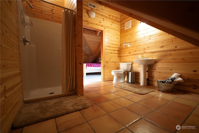 bathroom with wood walls, toilet, tile patterned floors, curtained shower, and sink