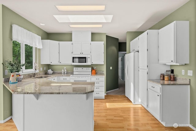 kitchen featuring white cabinets, white appliances, kitchen peninsula, and a skylight