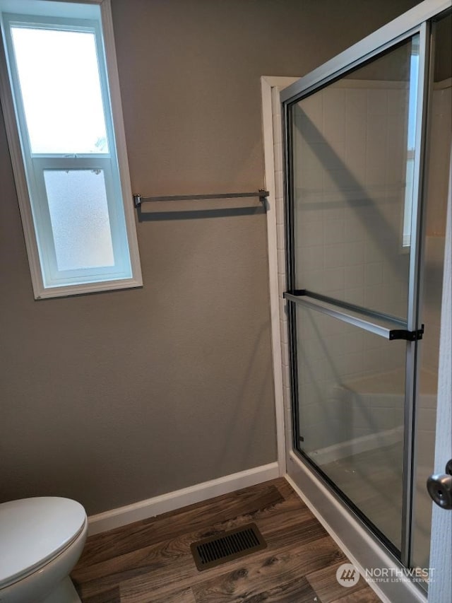 bathroom featuring hardwood / wood-style flooring, a shower with door, and toilet