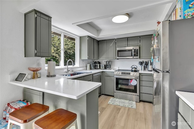 kitchen with kitchen peninsula, a breakfast bar, gray cabinetry, and appliances with stainless steel finishes