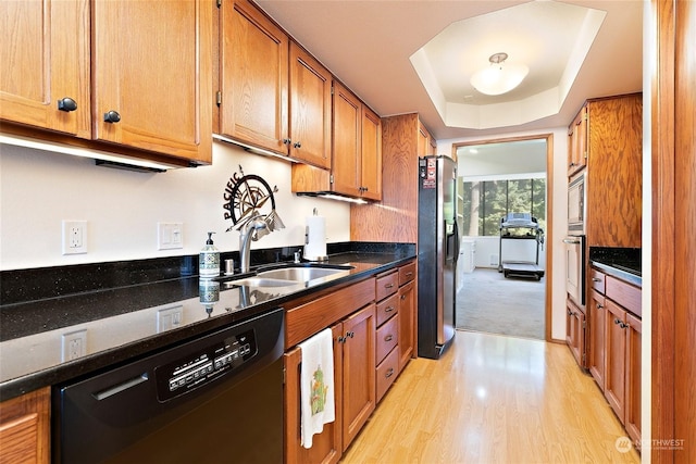 kitchen with appliances with stainless steel finishes, light hardwood / wood-style floors, a tray ceiling, and sink