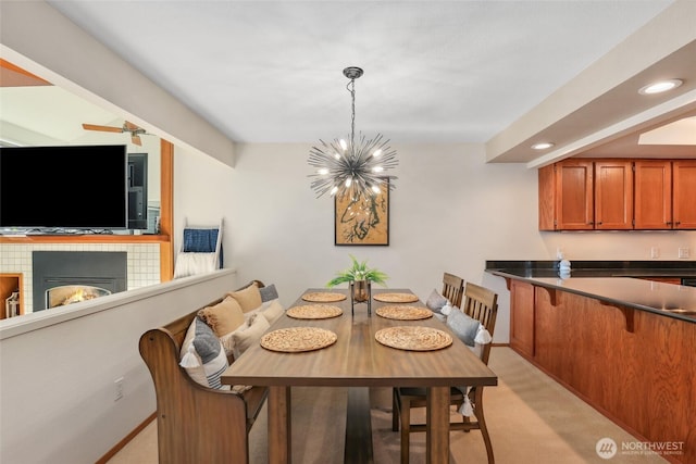 dining area with light colored carpet, ceiling fan with notable chandelier, and a tile fireplace