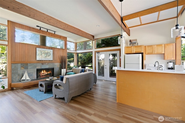 living room featuring beamed ceiling, sink, a tiled fireplace, a high ceiling, and light hardwood / wood-style flooring