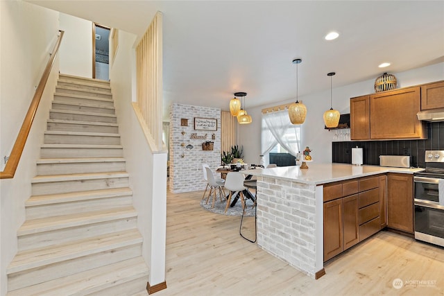 kitchen featuring tasteful backsplash, hanging light fixtures, light hardwood / wood-style flooring, and range with two ovens